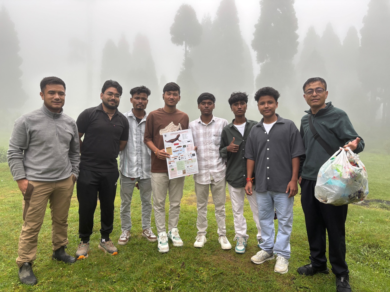 A group of young volunteers after a cleanup drive in the misty hills, holding collected waste